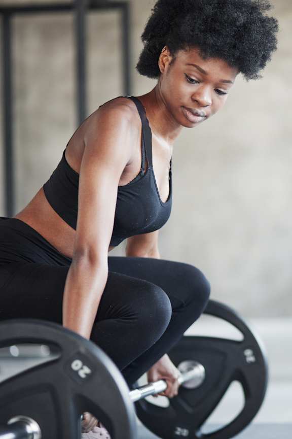 A woman with tattoos is doing pull-ups in a gym.