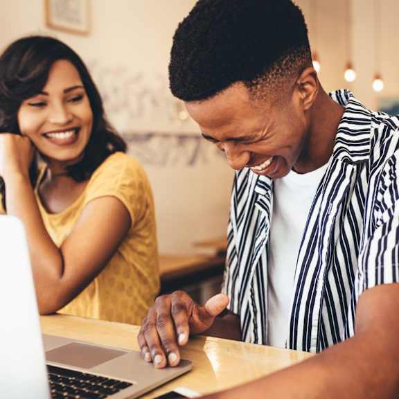 A man in a striped shirt is using a laptop while a woman looks on.