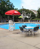 A poolside table with chairs and an umbrella is set up by a blue pool.