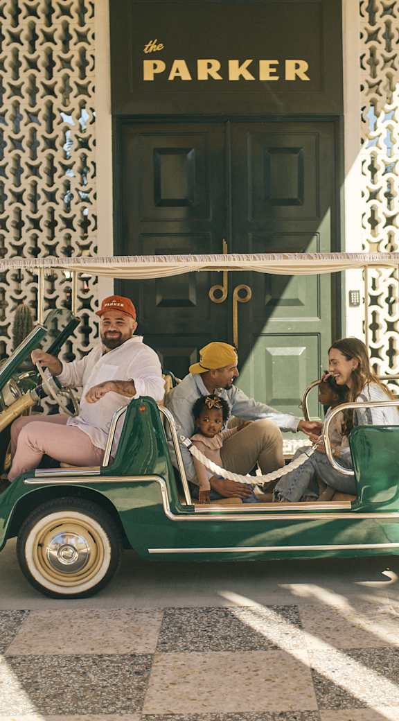 A green vintage car with four people inside is parked in front of a building with a sign that says  at The PARKER on E Mulberry Apartments, San Antonio, Texas