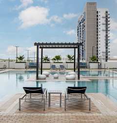 A pool area with a pergola and chairs in front of apartment buildings. at Palma, Doral, FL, 33166