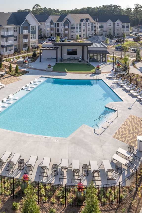 A large swimming pool surrounded by lounge chairs and a fence.