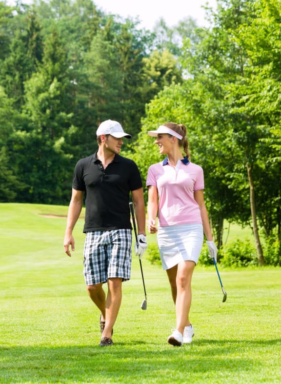 Man and Woman in Golf Attire Walking Along Golf Course