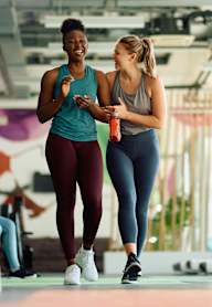 Two women walking and talking in a gym.