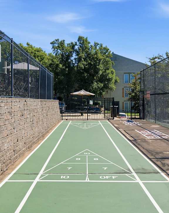 A basketball court with a green surface and white lines is surrounded by a black fence.
