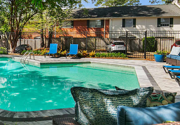 A pool surrounded by trees and chairs.