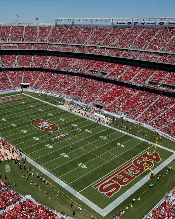 A stadium full of red seats with a football game taking place.