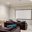 A living room with a couch, a chair, and a white screen on the wall.