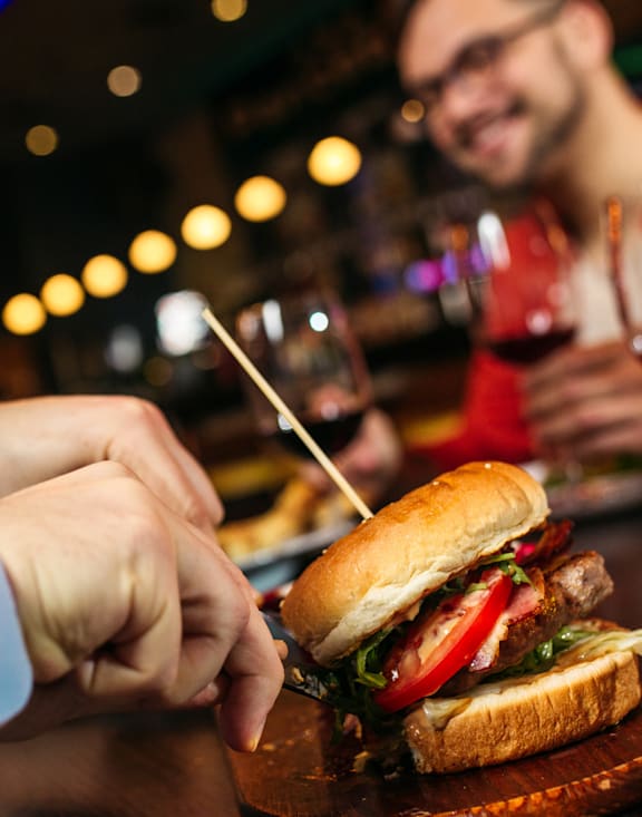 A man in a blue shirt is pointing at a sandwich on a wooden board.