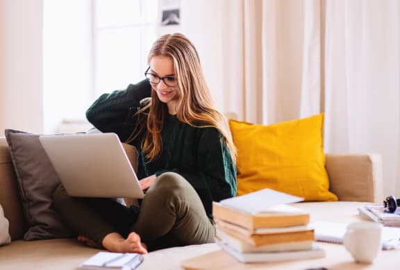 A young happy college female student sitting on sofa at home, using laptop when studying. at Renaissance Park Apartments, Davis, CA