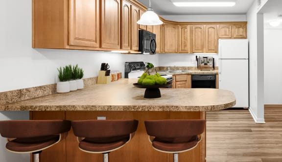 A kitchen with granite countertops, bar stool seating, upgraded lighting, black & white appliances, and hardwood floors.