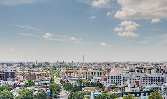 A cityscape with buildings and trees under a blue sky with clouds.