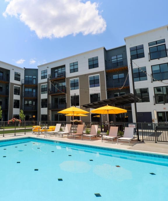 a swimming pool with yellow umbrellas in front of an apartment building