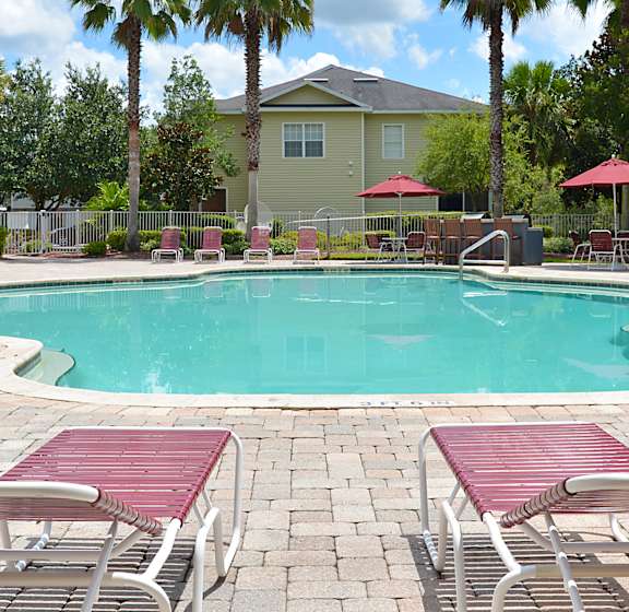 A pool surrounded by red lounge chairs and palm trees.