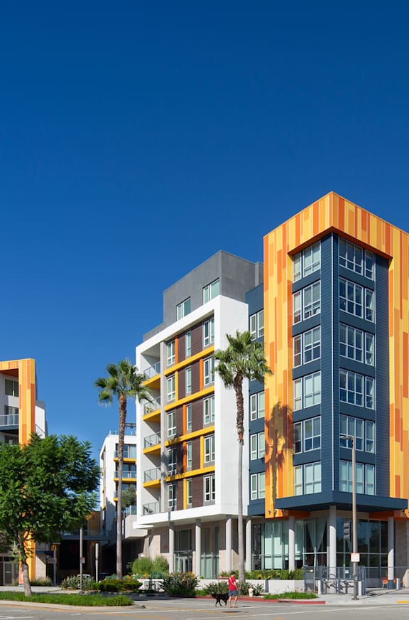 A modern multi-story building with orange and white accents stands in the foreground of a parking lot.