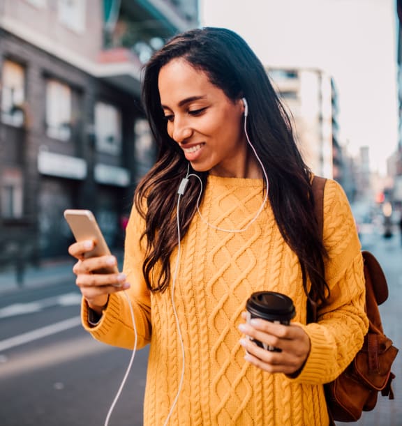 a woman walking down the street looking at her cell phone and holding a coffee cup