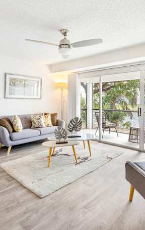 A living room with a grey couch, a grey armchair, a white rug, and a ceiling fan.