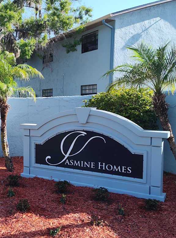 A white sign that says "Jasmine Homes" in front of the apartments.