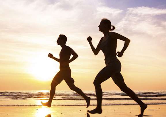Two people running on the beach at sunset.