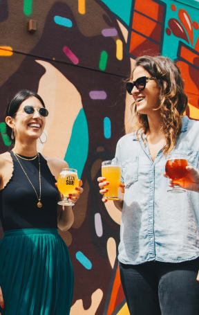 a group of women standing in front of a mural holding drinks