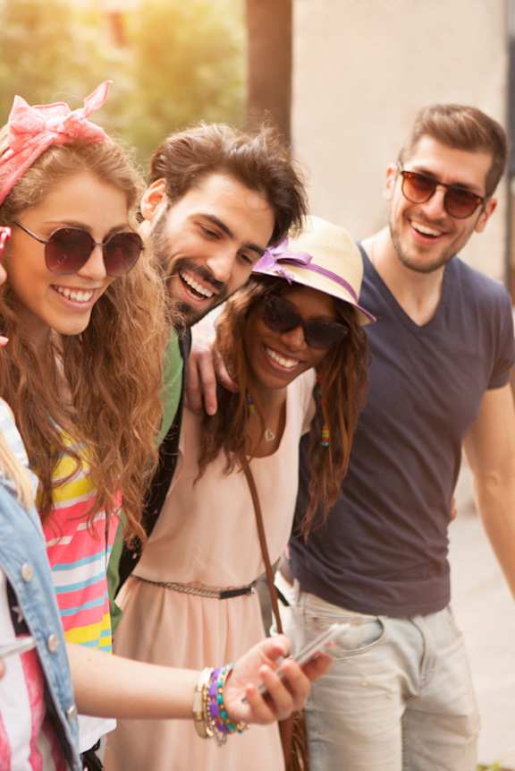 A woman with curly hair wearing sunglasses and a yellow sweater is holding shopping bags.