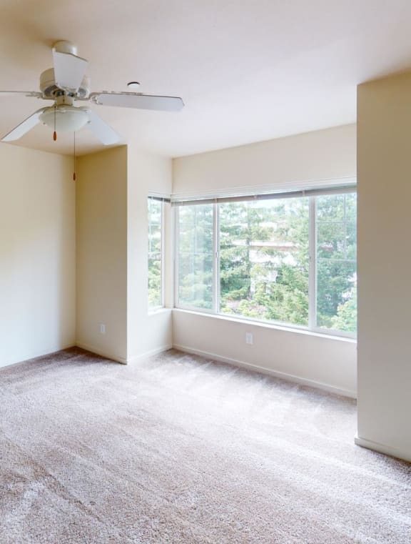 an empty living room with a large window and a ceiling fan