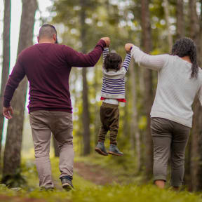 a family walking through the woods holding hands and a child jumping