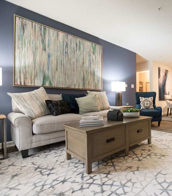 A living room with a white couch, a wooden coffee table, and a large abstract painting on the wall.