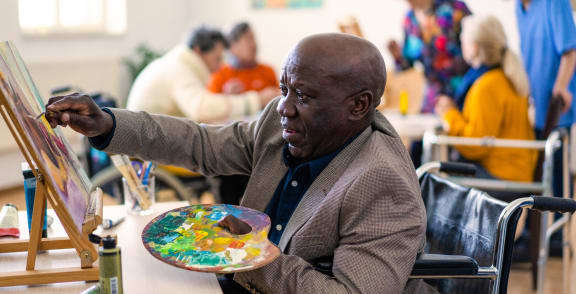 a man sitting at a table holding a plate of art in front of a canvas