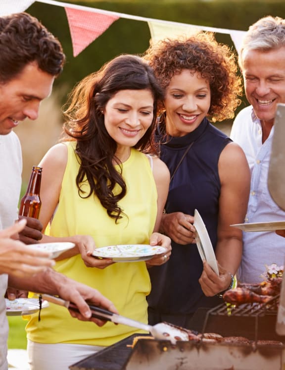 Group of Adult Friends Standing Around Outside BBQ Getting Food