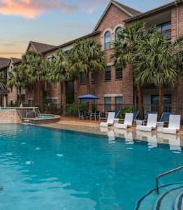 A swimming pool surrounded by palm trees and lounge chairs.