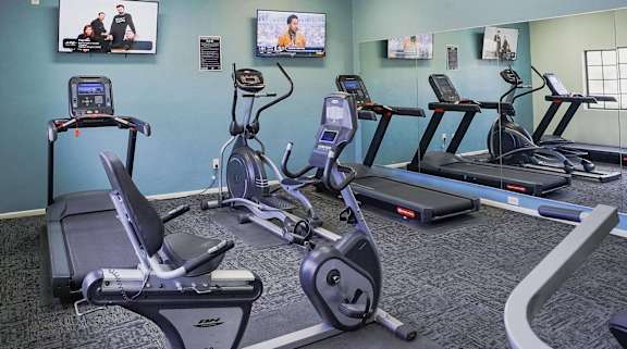 A gym with treadmills, exercise bikes, and a television.