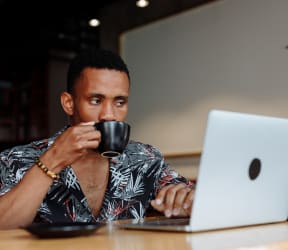 a man sitting in front of a laptop drinking a cup of coffee at Missouri Crossing, Phoenix, Arizona