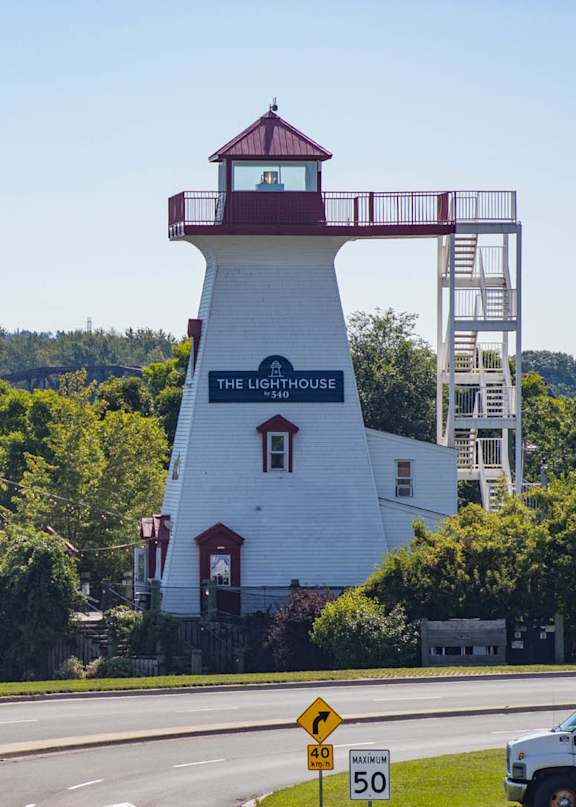 A white lighthouse with a red roof stands on the side of a road.
