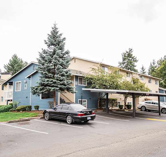 A car is parked in a parking lot in front of a blue building at Ellyson Apartment Homes in Tacoma, WA