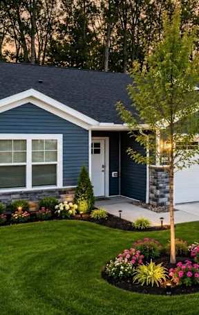 A blue house with a white garage door and a tree in the front yard.