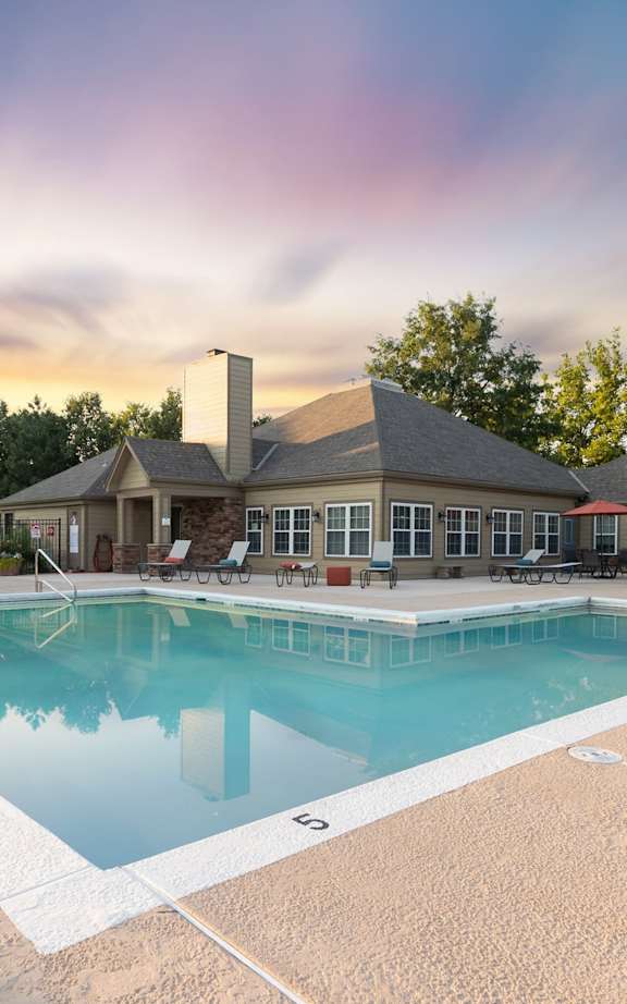 Large outdoor swimming pool surrounded by a concrete patio and lounge chairs at The Lakes Apartments.