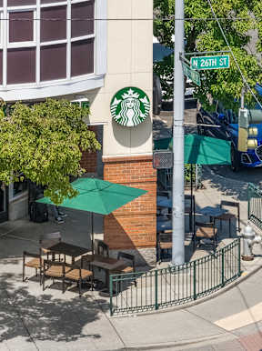 A Starbucks sign is on a pole at the corner of a street.