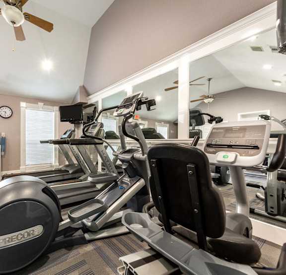 A gym with a variety of equipment including treadmills, elliptical machines, and a fan.