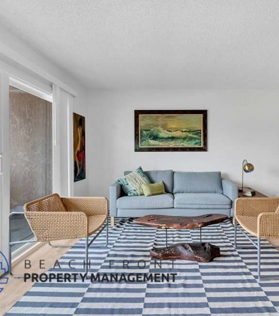 A living room with a grey couch and a painting on the wall.