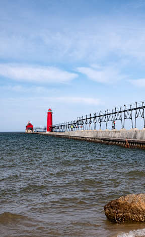 A red lighthouse stands on a pier in the middle of the ocean. at Ventura Townhouses, Michigan, 49460