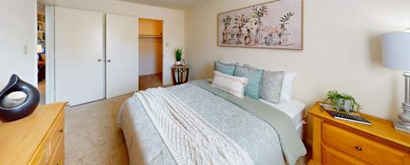 A bedroom with a bed, nightstand, and a painting on the wall.