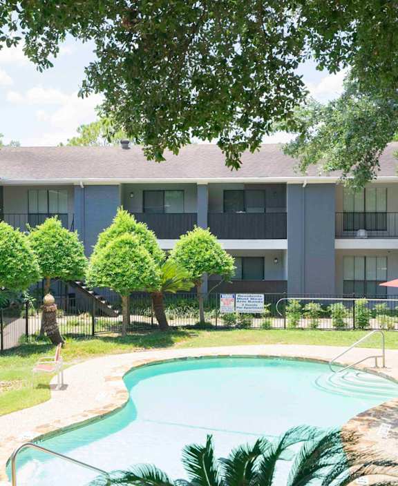 A swimming pool is surrounded by a grassy area and trees.