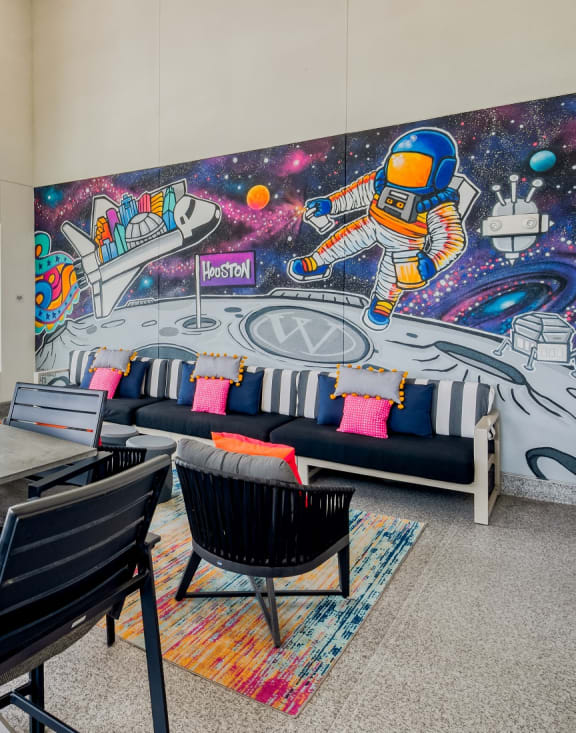 a communal area with a table and chairs and a mural on the wall