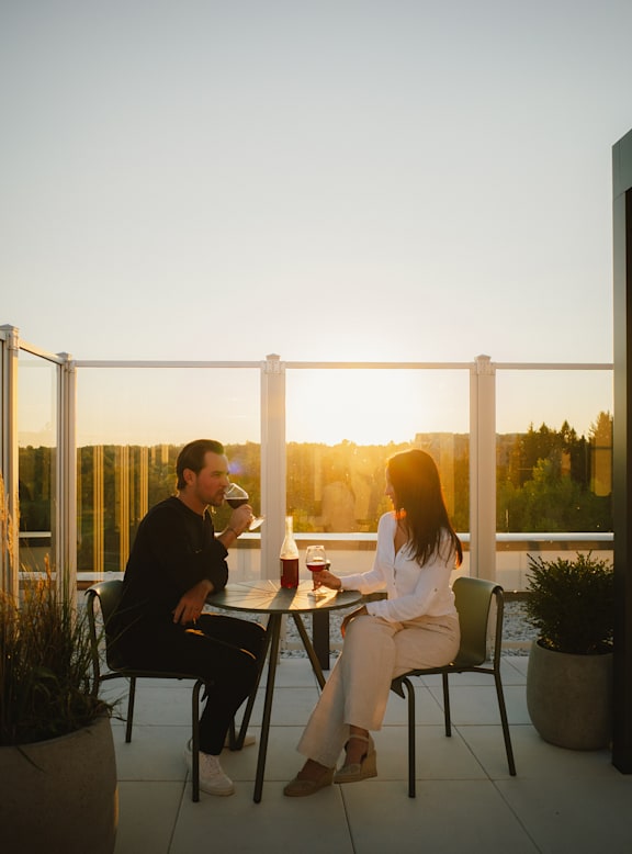 Two people sitting at a table on a balcony during sunset.