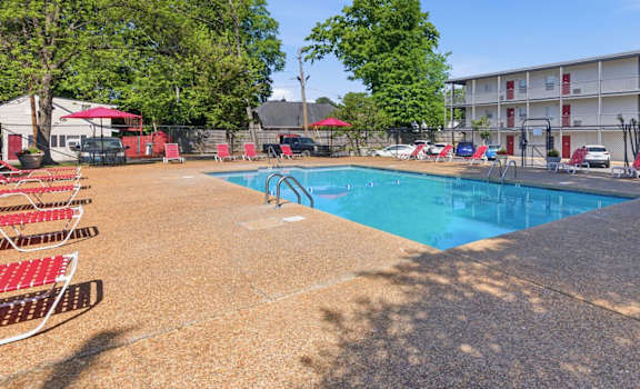 A swimming pool surrounded by red chairs and trees.