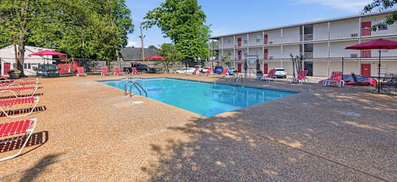 A swimming pool surrounded by red chairs and trees.