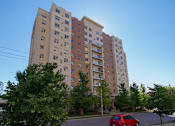 Thumbnail 5 of 33 - A red car is parked on the street in front of a tall apartment building.