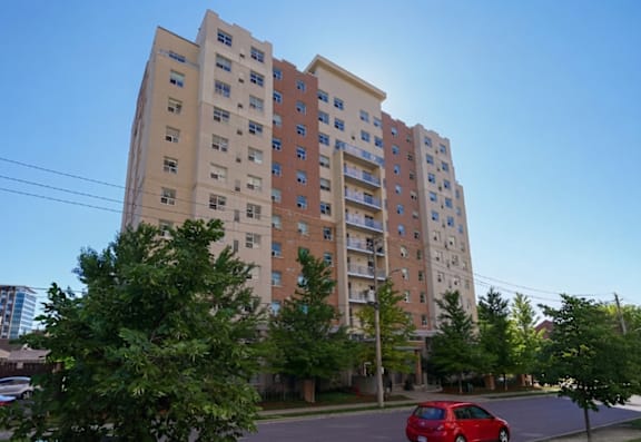 A red car is parked on the street in front of a tall apartment building.