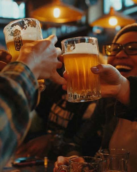 people sitting at a bar holding up glasses of beer